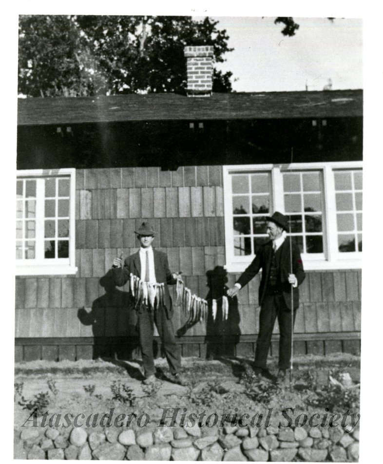 Black and white photograph of two men holding a stringer of fish.