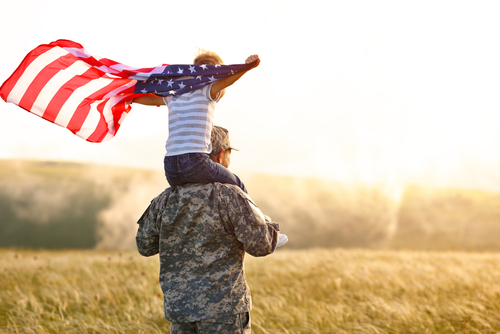 Rear view of military man father carrying happy little son with american flag on shoulders and enjoying amazing summer nature view on sunny day_ happy male soldier dad reunited with son after US army