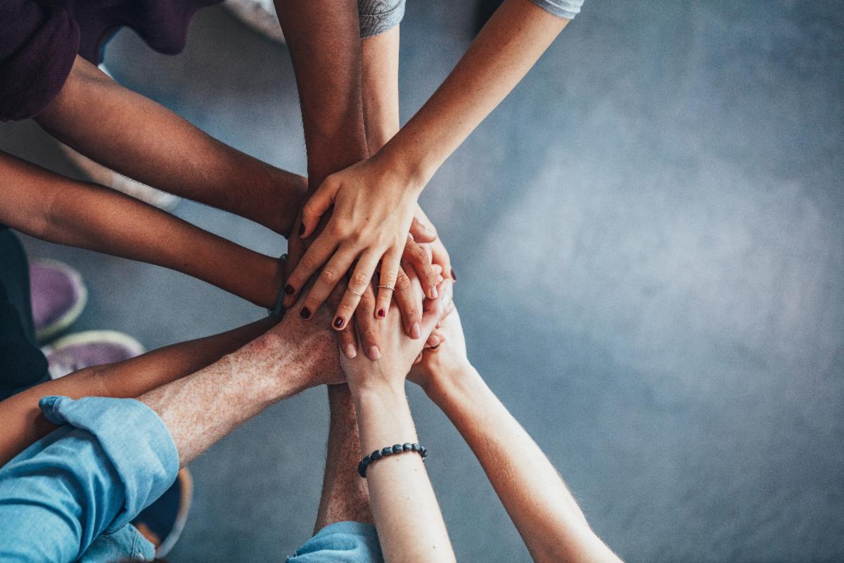 11 hands coming together in the center. Hands belong to individuals of different ages, genders, races. An image of inclusion and community