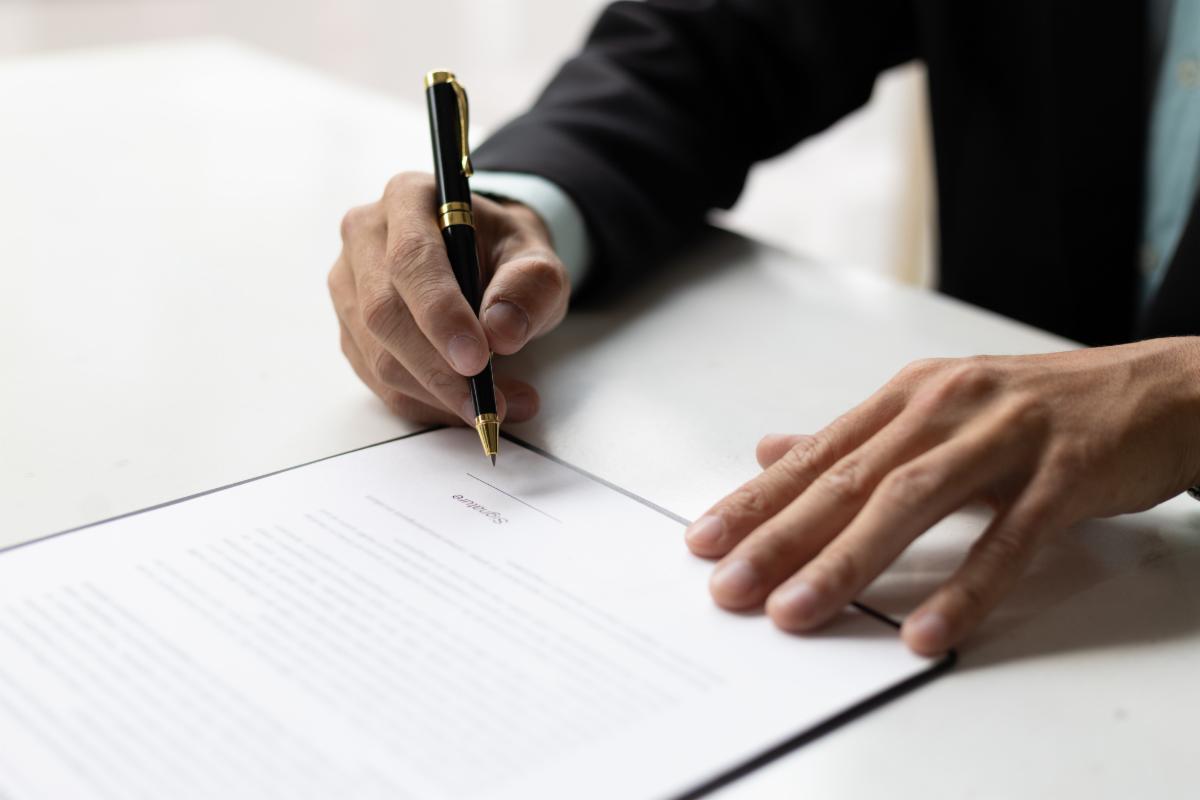 Close up man wearing a suit signing a document with a black and gold pen.