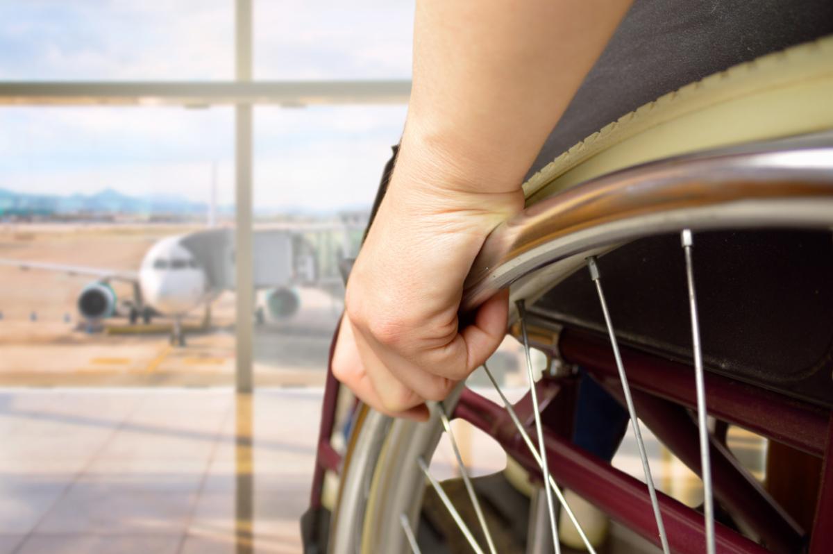 wheelchair user in foreground facing view of passenger planes through window.