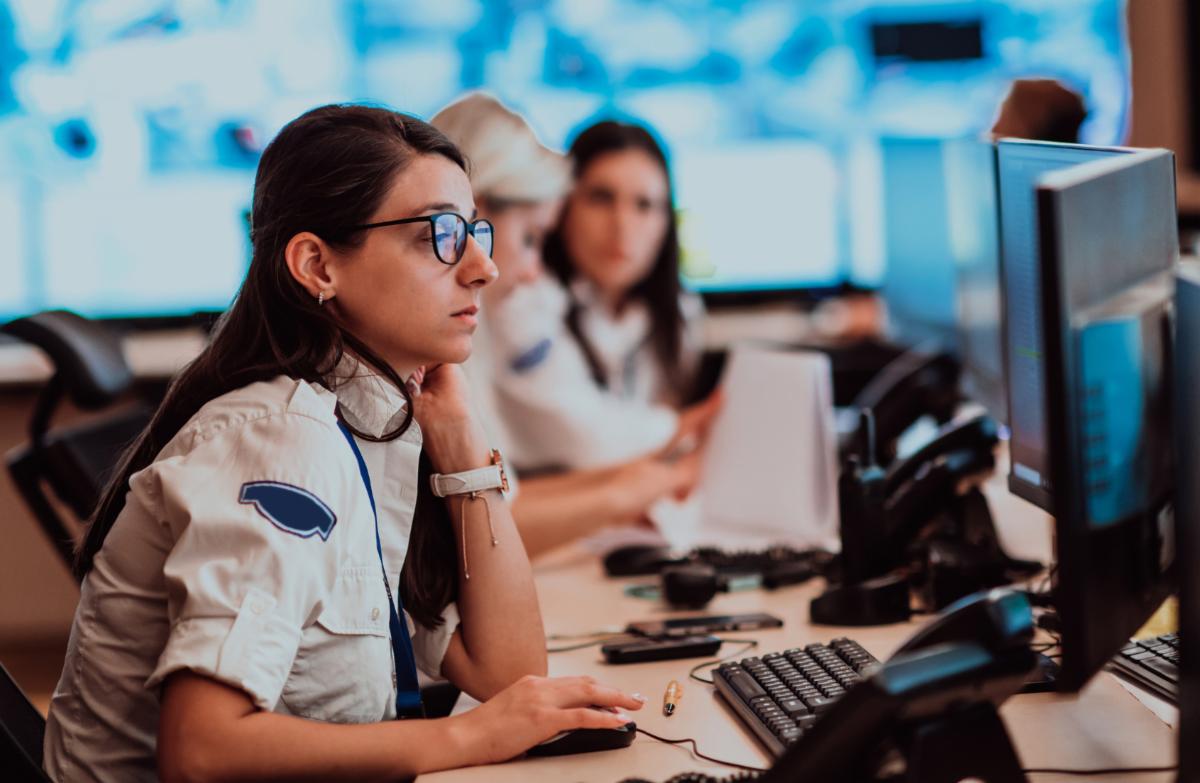 Female 911 responder taking calls at a busy emergency response center.