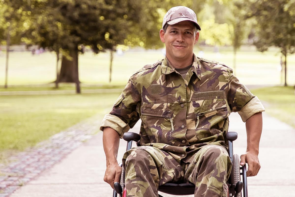 Veteran wheelchair user wearing camouflage and smiling for camera.
