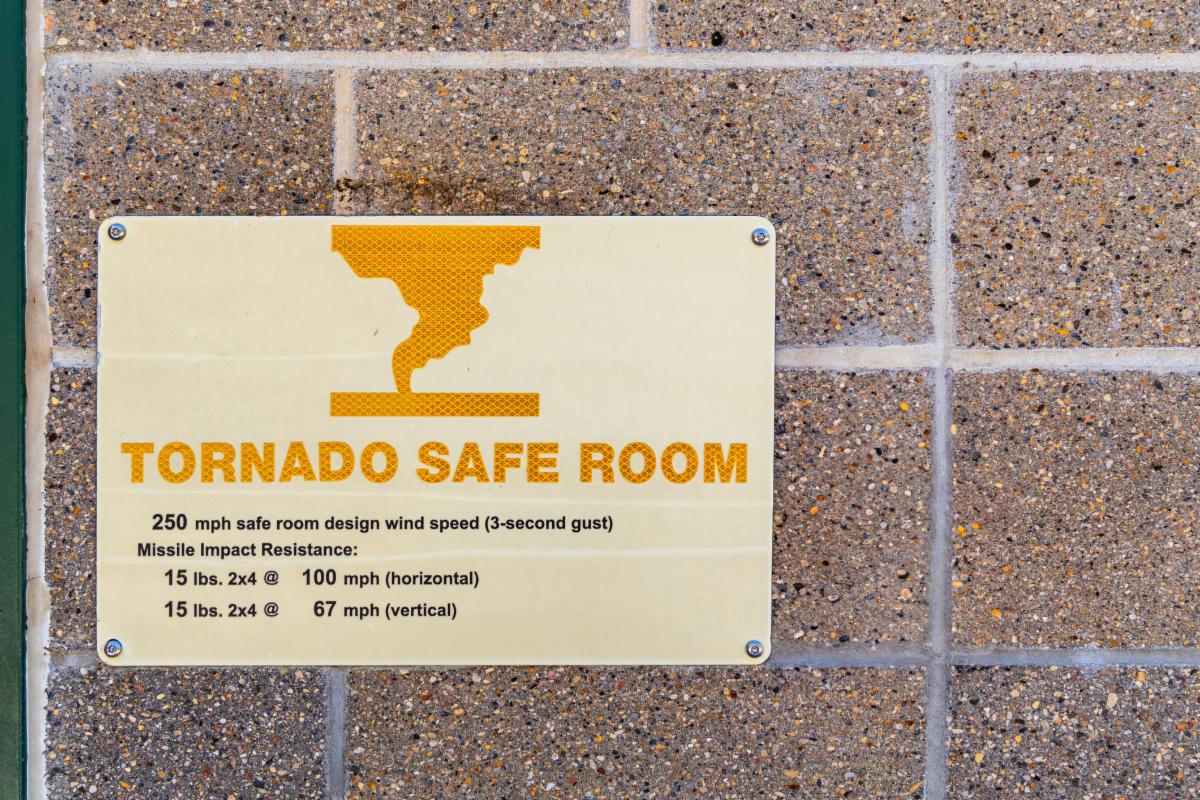 Sign that reads Tornado Safe Room on side of brick wall.