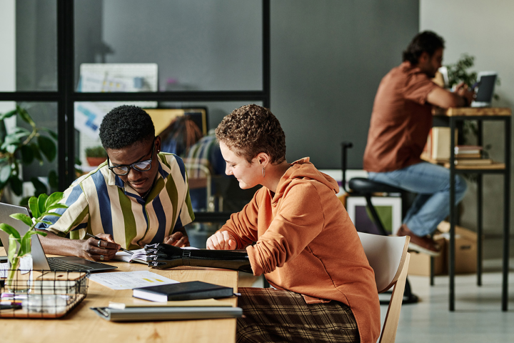 Two young people looking over employment information at a table. One is a young black male and the other is young woman with a prosthetic arm and hand.
