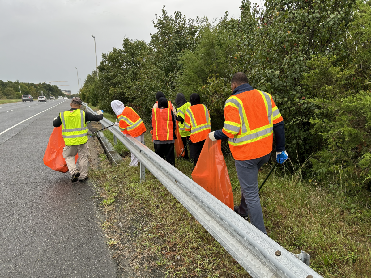 Group in safety vests walks next to road. 