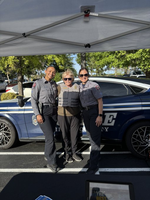 Two police officers pose with a person in front of a car. 