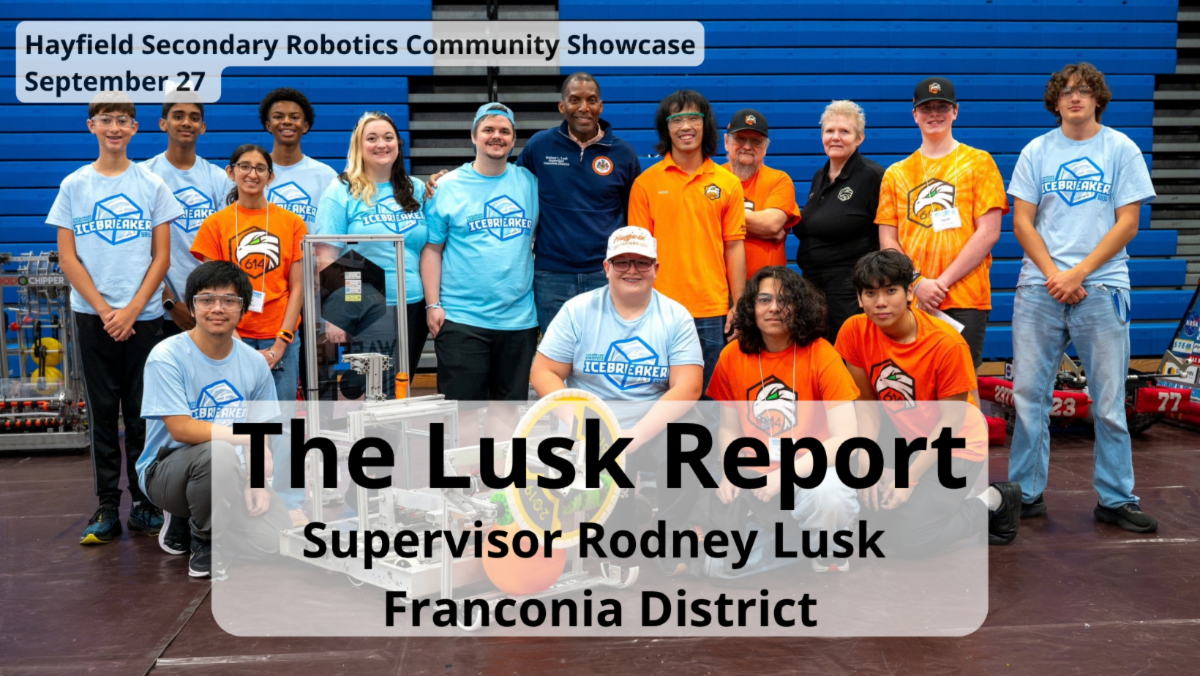 Group poses in front of robot with "Lusk Report. Supervisor Rodney Lusk Franconia District" written on top. 