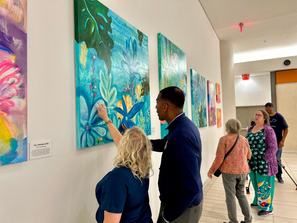 Two people observe a painting on a wall.