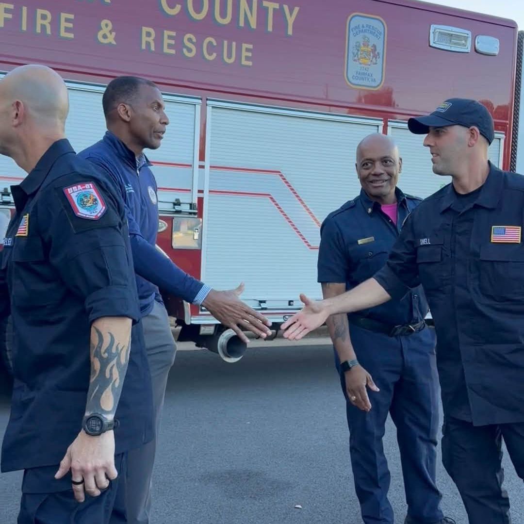 Men stand and shake hands in front of a fire truck.