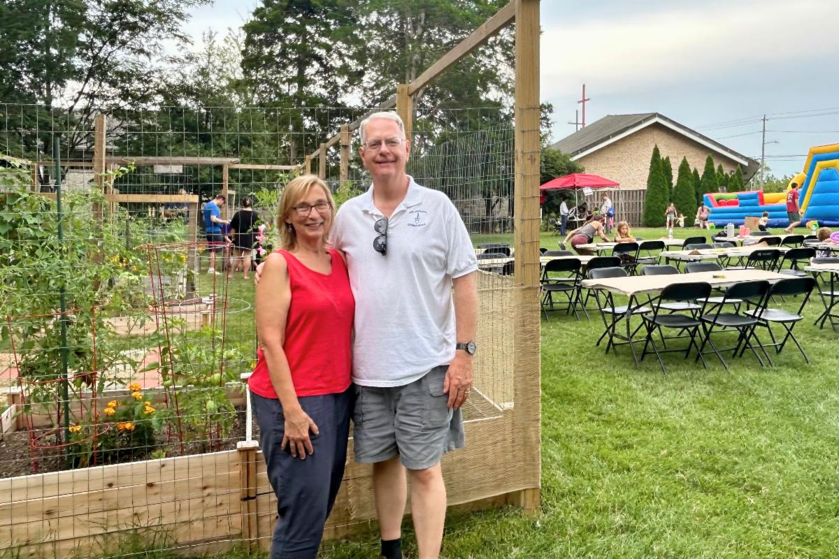 Man and woman pose in front of garden bed. 