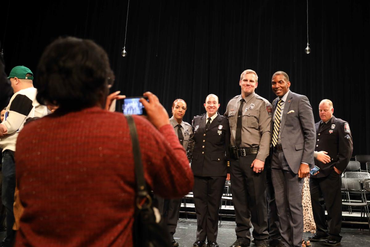 Woman takes photo of four people posing on stage.