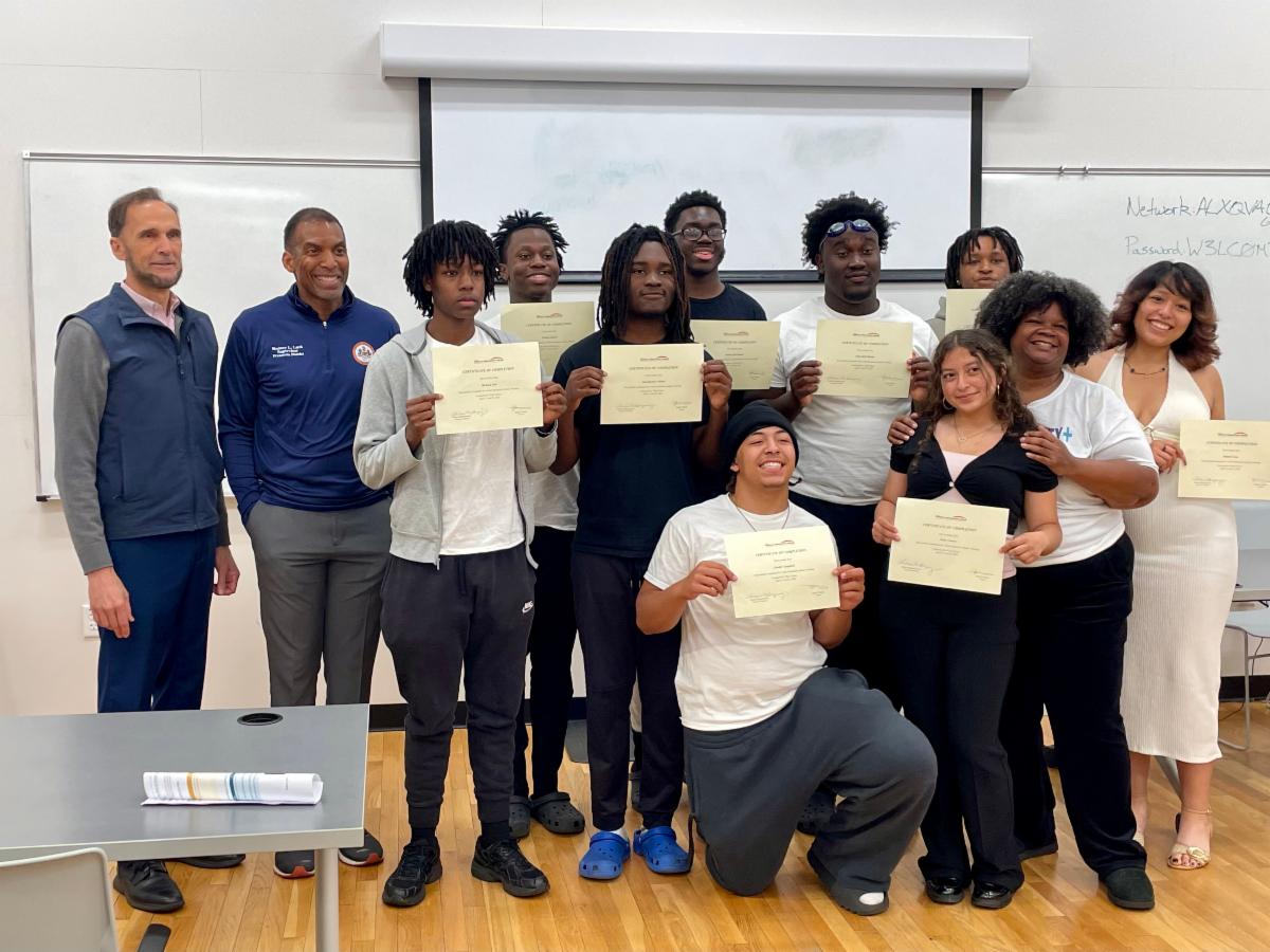 Group of students and staff pose in a classroom, proudly holding certificates after completing a program.