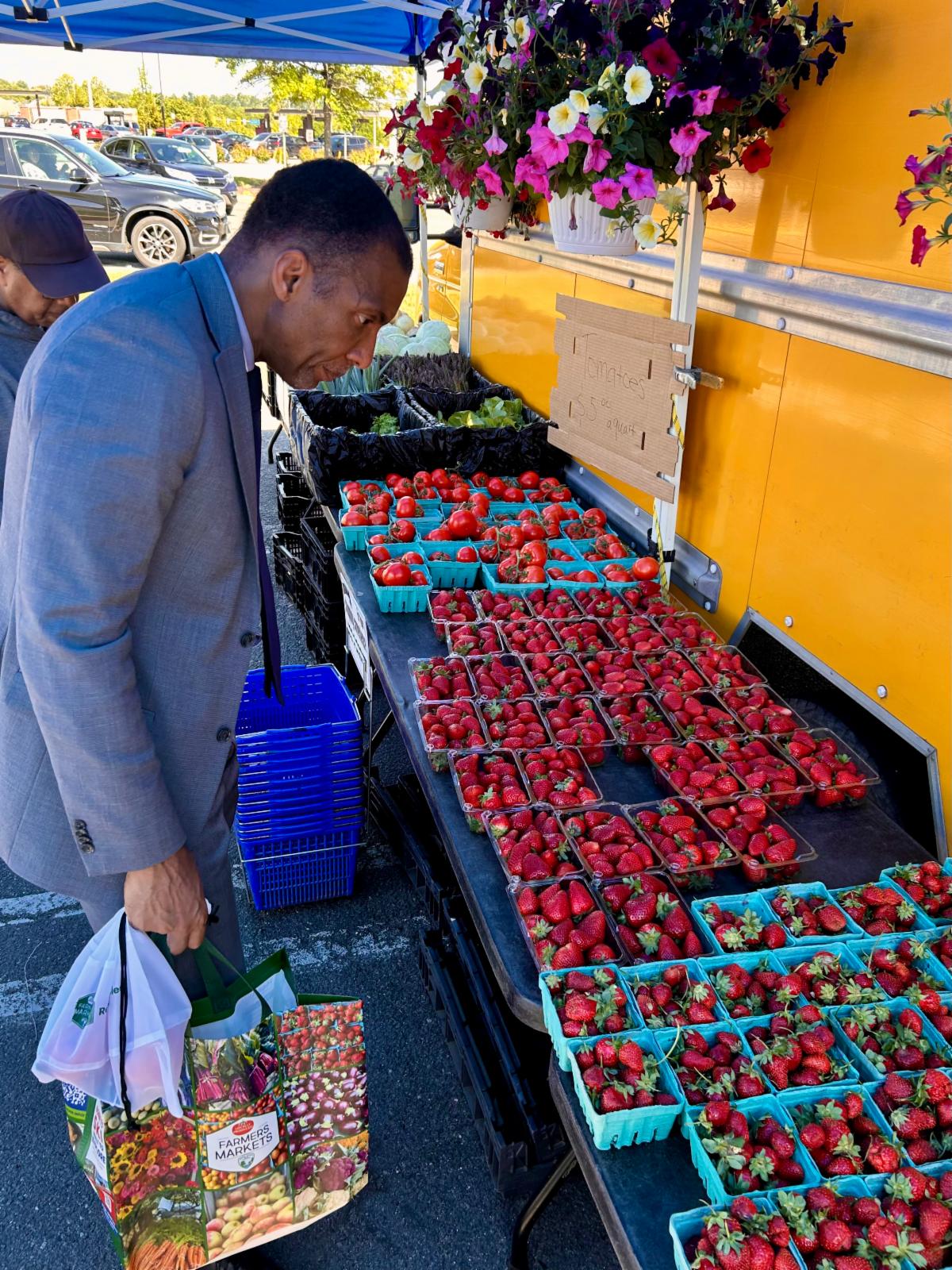 Person with a reusable bag examines rows of baskets filled with strawberries at a farmers market stand.