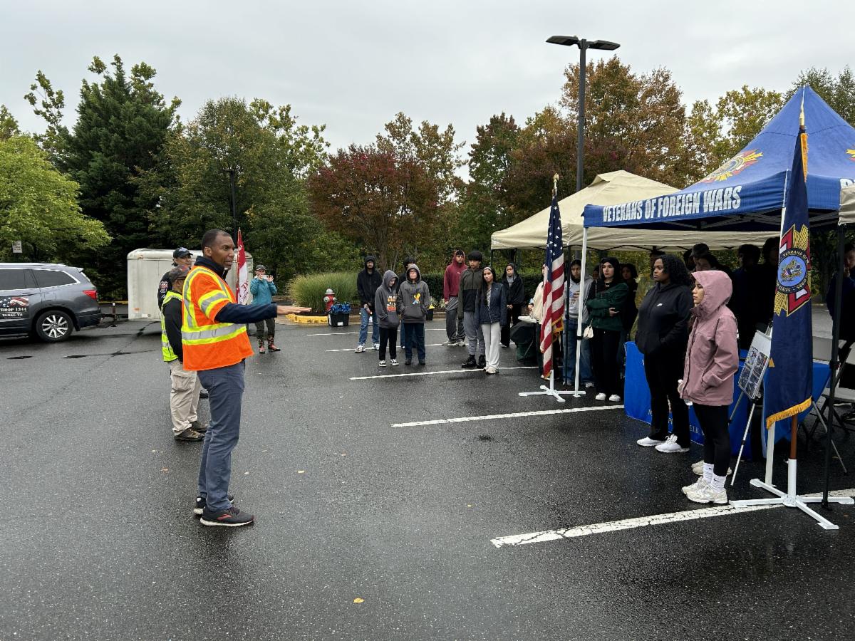Man speaks to group standing under tent. 