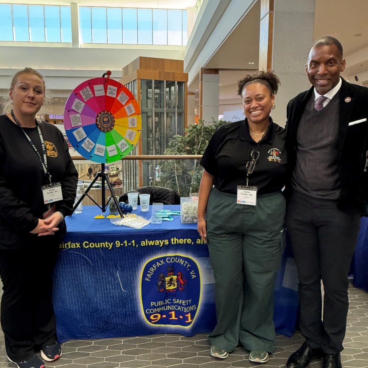 Three people pose next to table with 911 communications information.