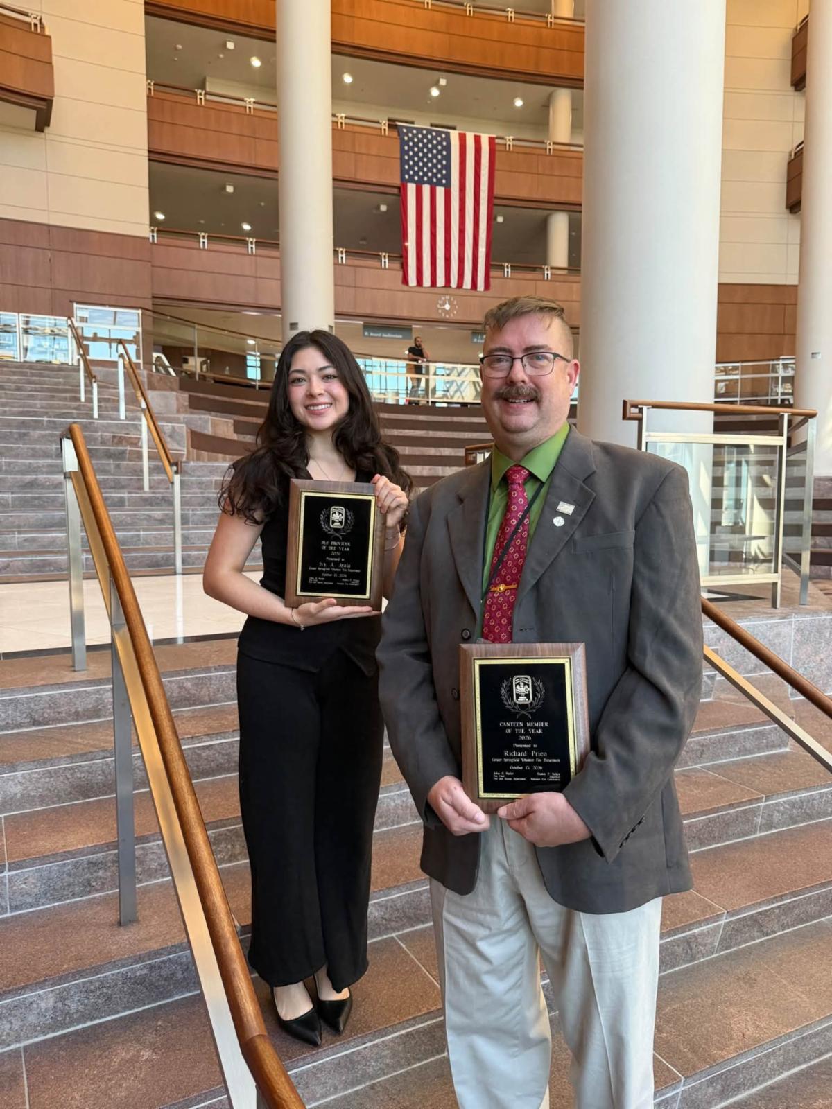 Man and woman hold plaques and stand on stairs.