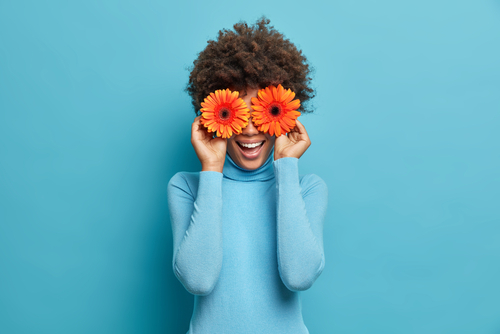 Playful positive African American woman covers eyes with two orange gerb...