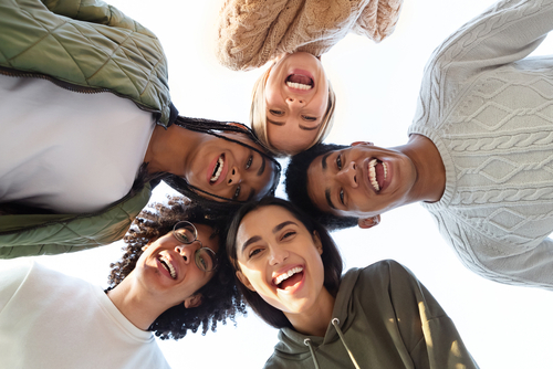 Smiling multiracial group of young friends forming circle of heads and l...