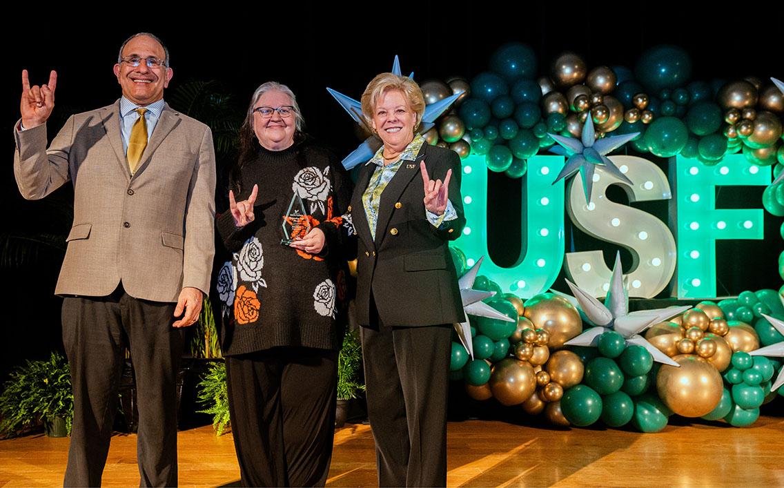 Janet Reyes accepting award on stage with USF President