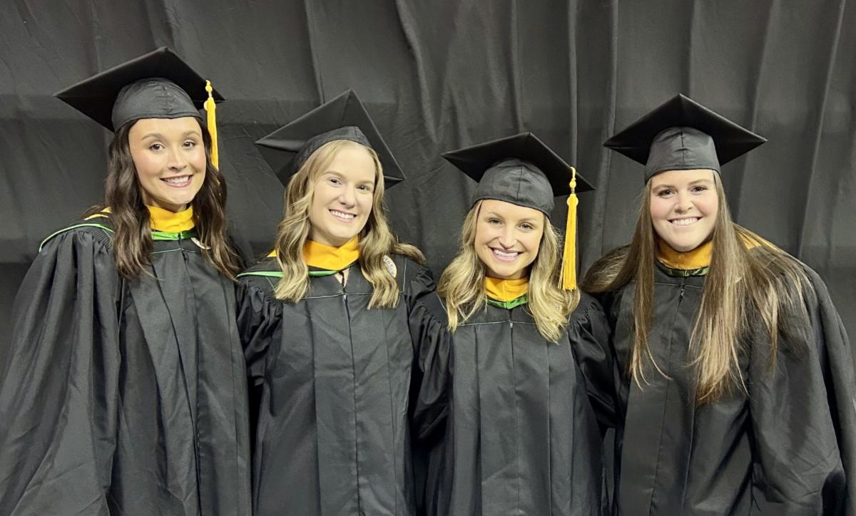 4 graduates looking at camera in cap and gown