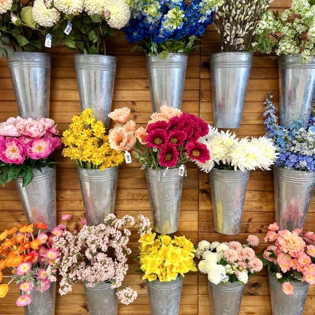 flowers in metal vases hanging on a wooden wall