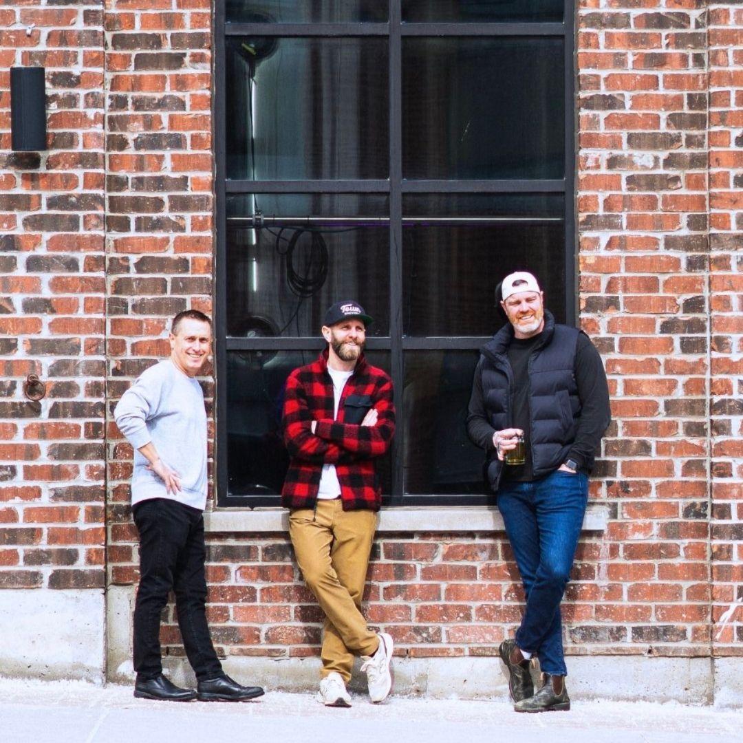 three men lean against the exterior of a building