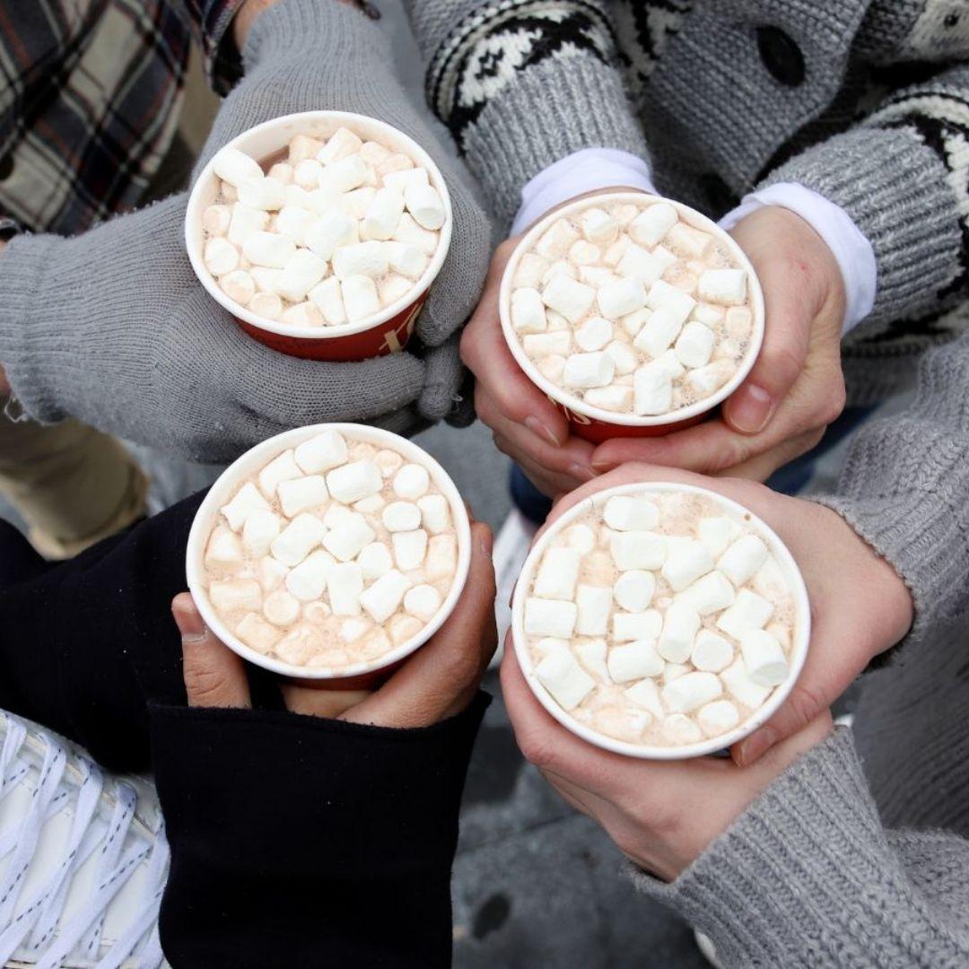 four pairs of hands holding up cups of hot chocolate with  marshmallows