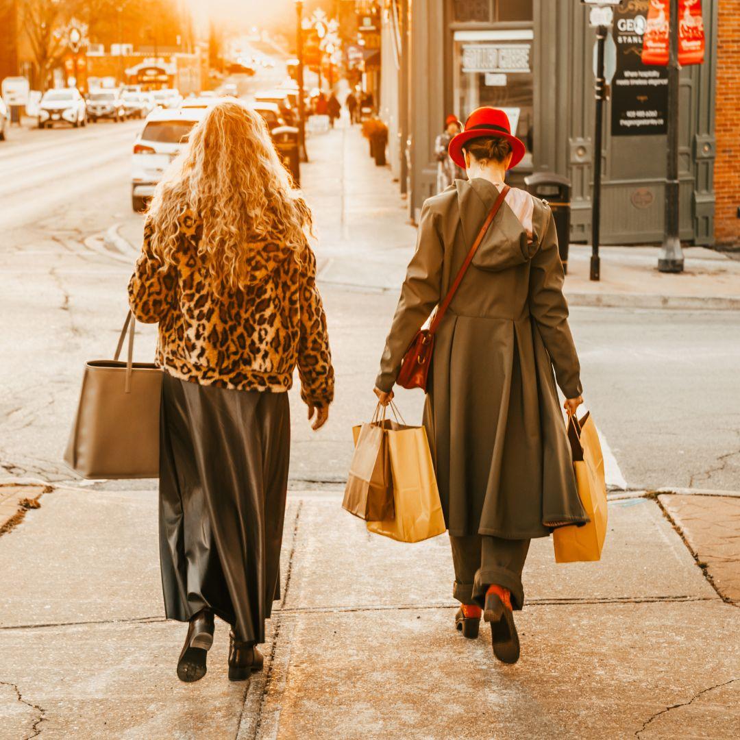 two women carrying shopping bags walk down a main street