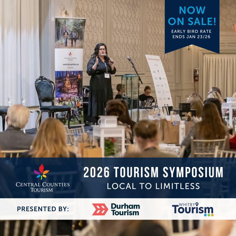 woman stands on stage speaking to a crowd of people seated at tables. Central Counties Tourism logo on bottom left with text: 2026 Tourism Symposium, local to limitless. partner logos on bottom