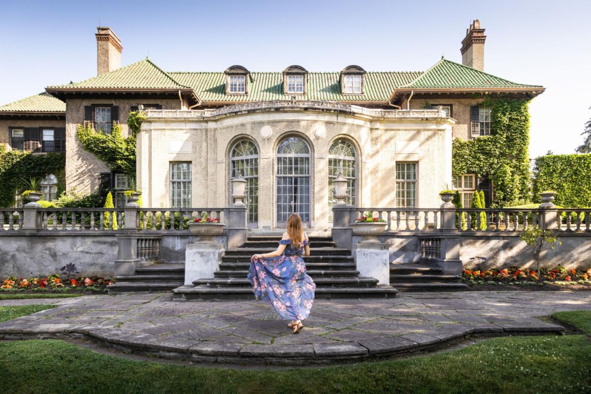 woman stands before a large historic house