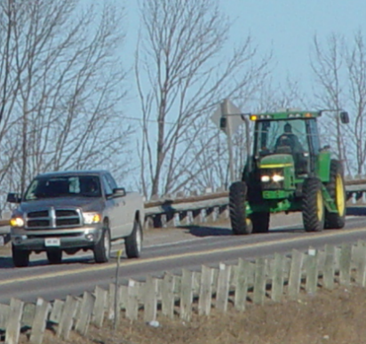 Image of a car and farm vehicle driving along a road.