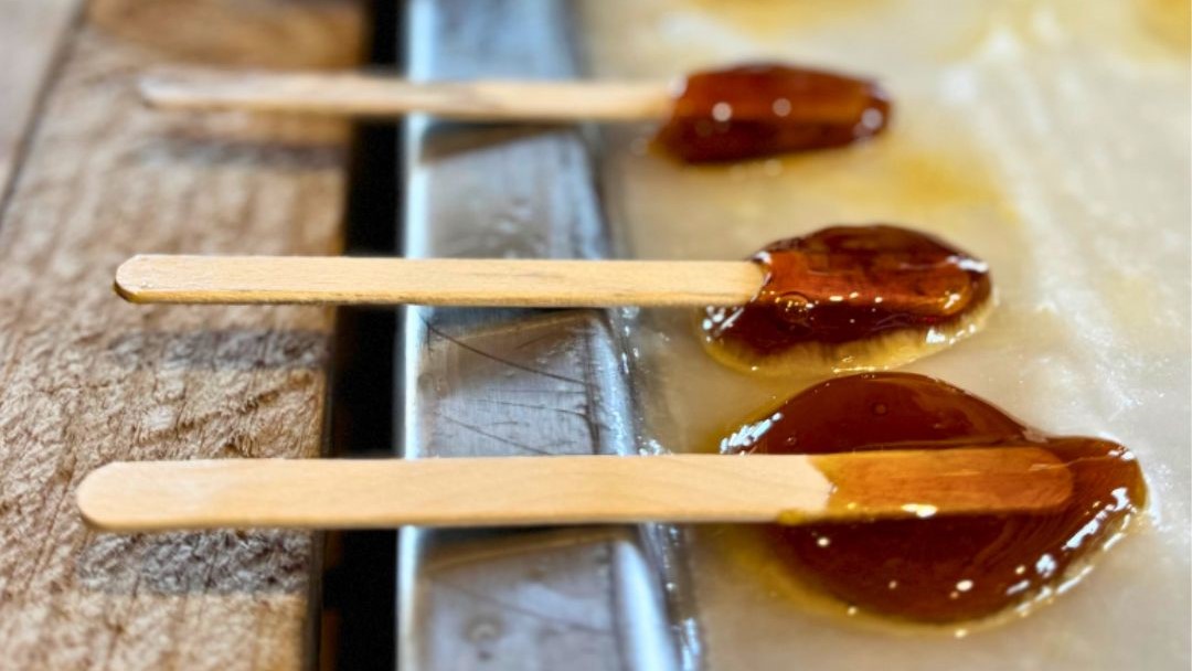 3 popsicle sticks with maple taffy laid out on a flat surface 