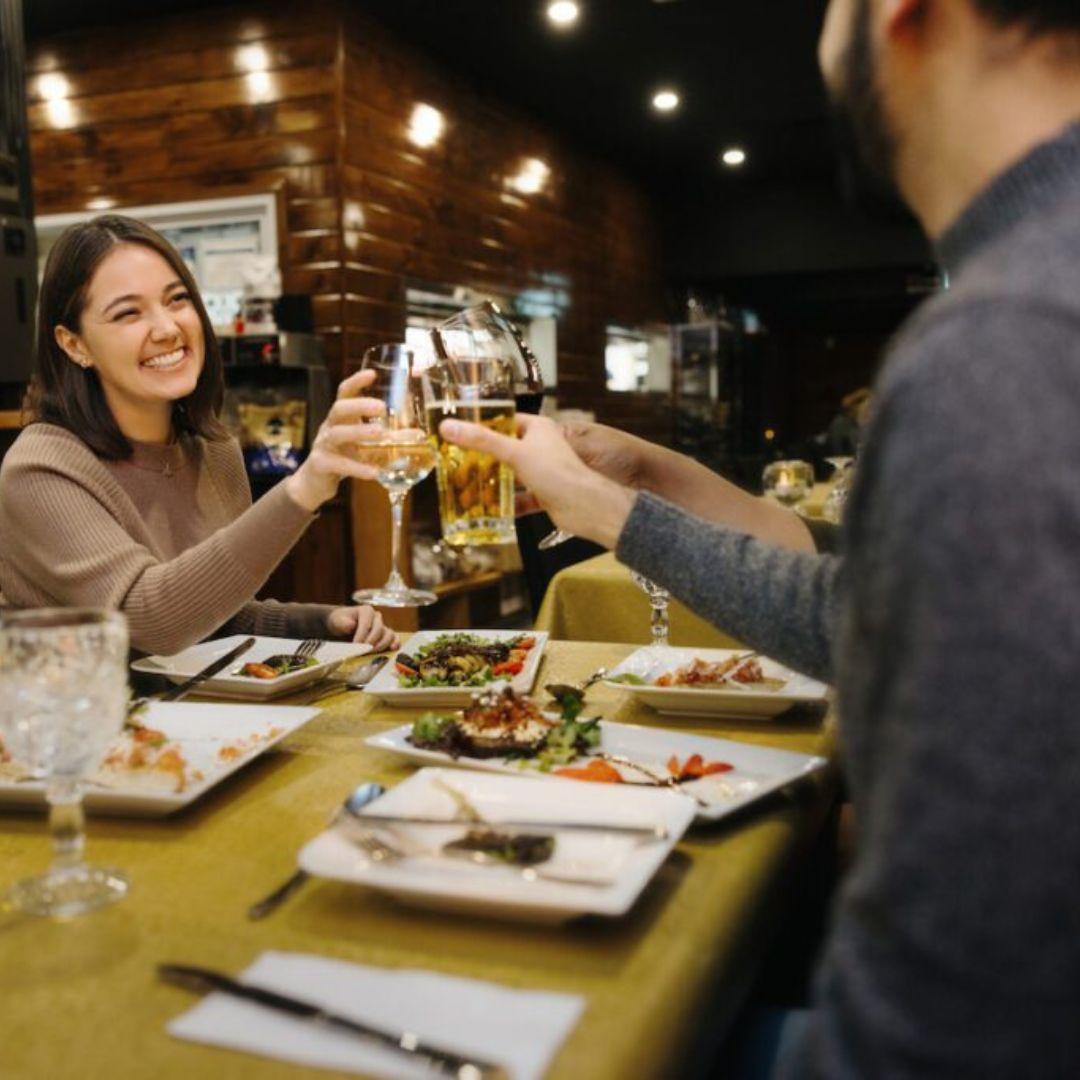 man and woman clinking drinks over a meal at a restaurant