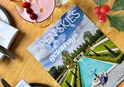 Open Skies adventure planner on a table alongside food and drink