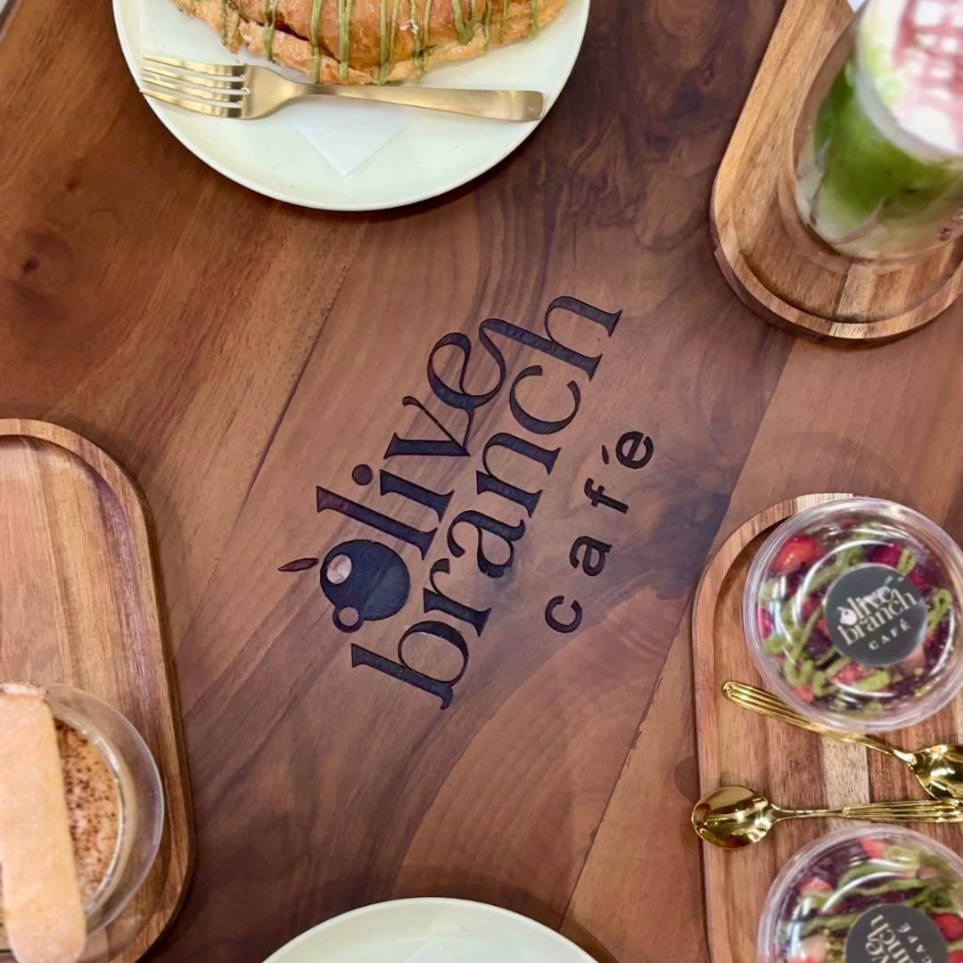 Olive Branch Cafe logo on a wooden table surrounded by plates of food and drinks