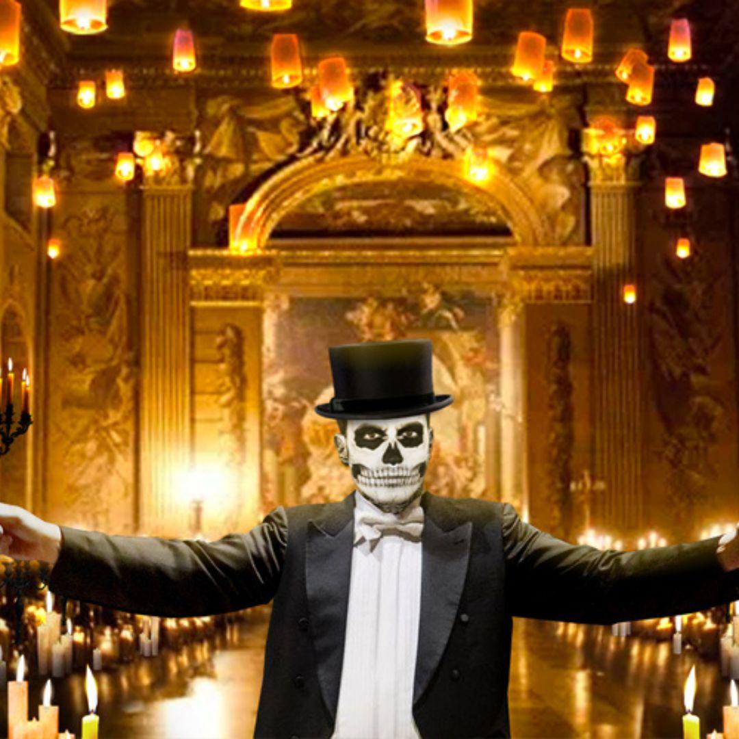 Person dressed in a suit and top hat and wearing a skeleton mask stands with their arms outstretched with candles burning behind them.