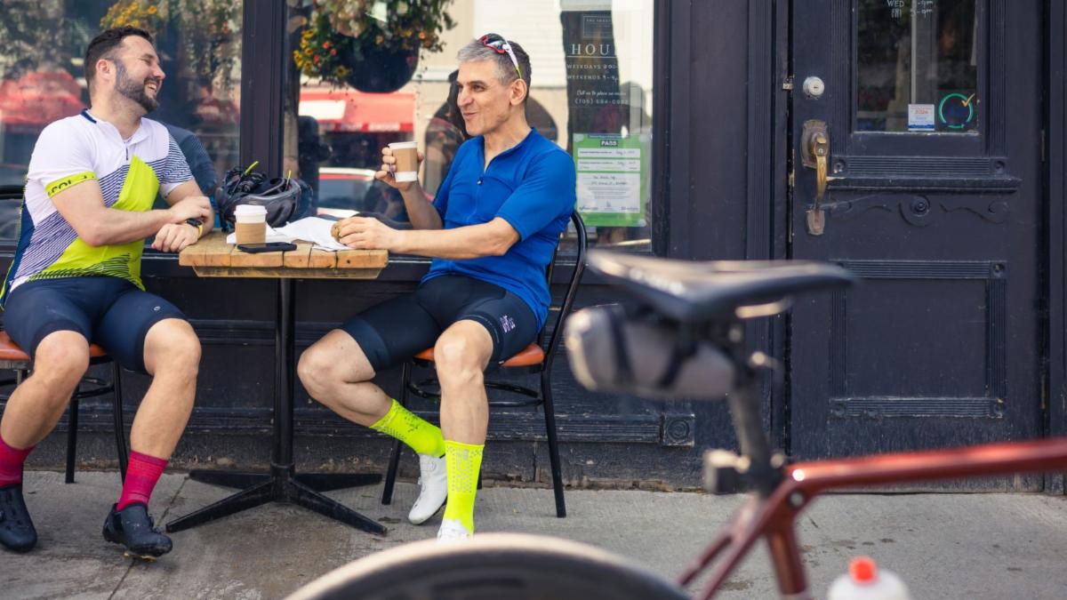 Two men seated at an outdoor cafe with a bike in the foreground