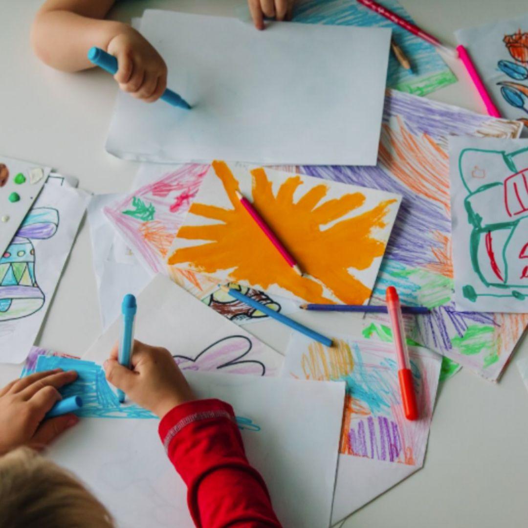 Children's hands shown drawing at a table full of art