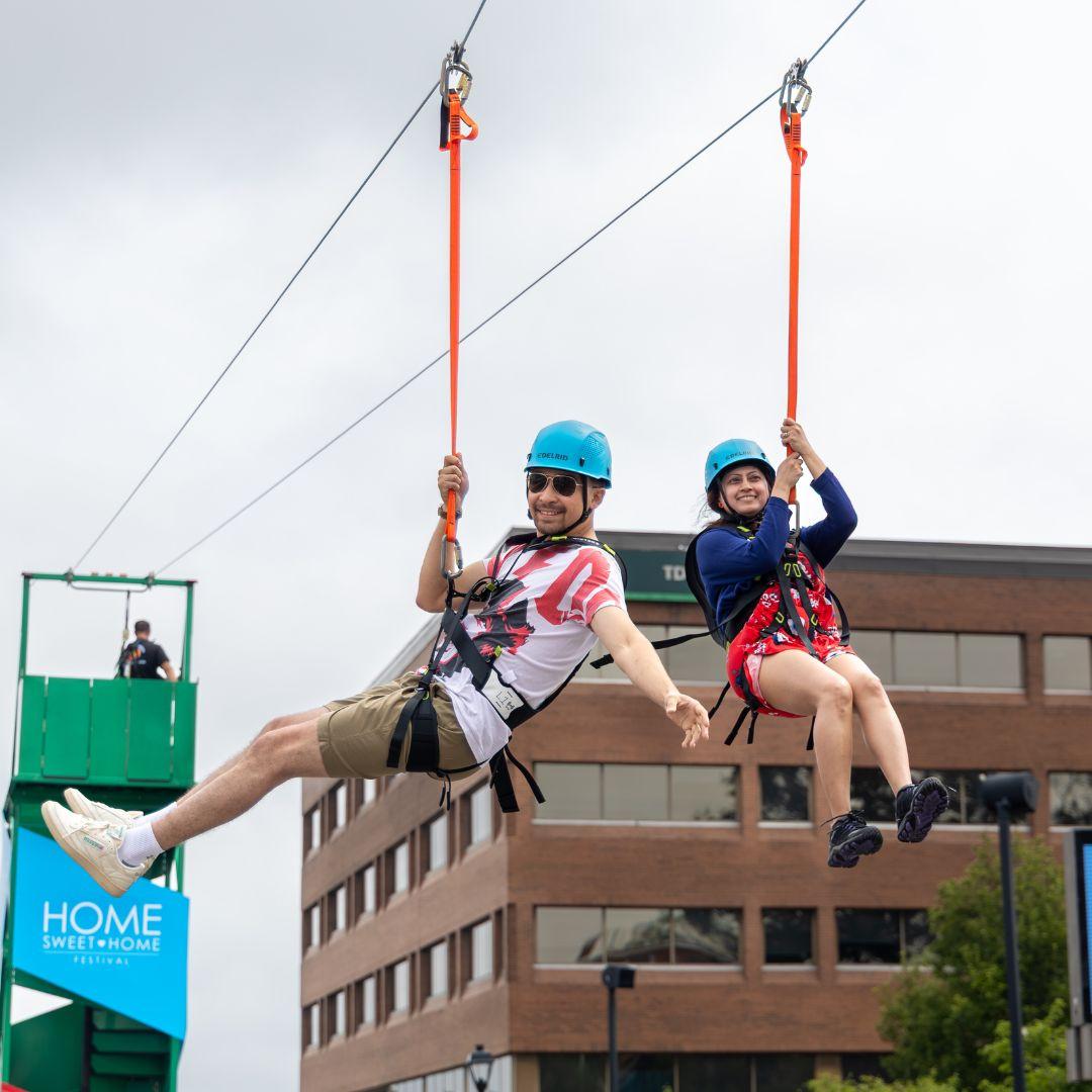 two people ziplining across downtown street