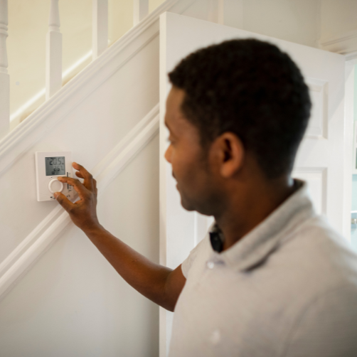 A person standing in front of a door adjusting a thermostat on the wall.