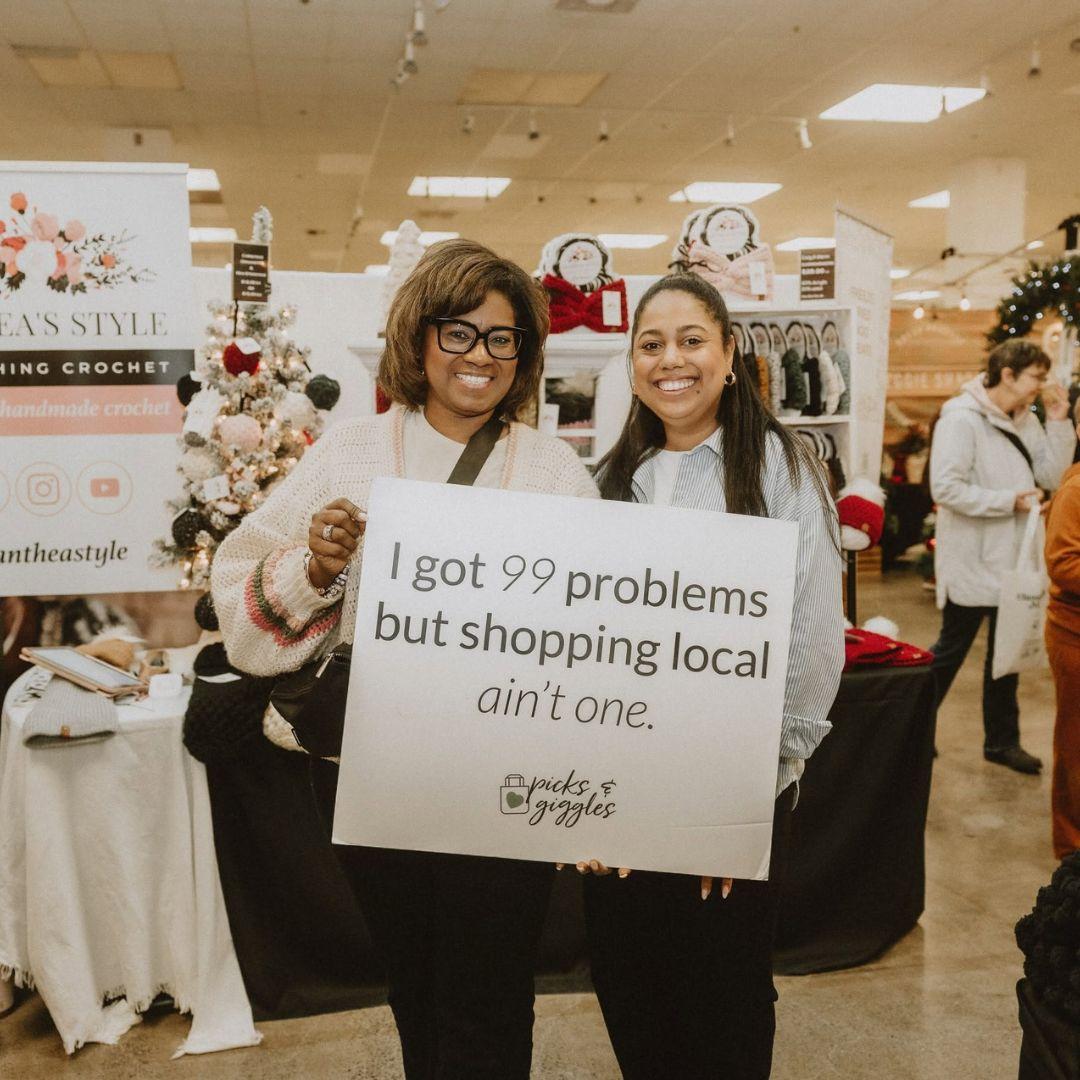 two women stand in a store holding up a sign promoting local shopping