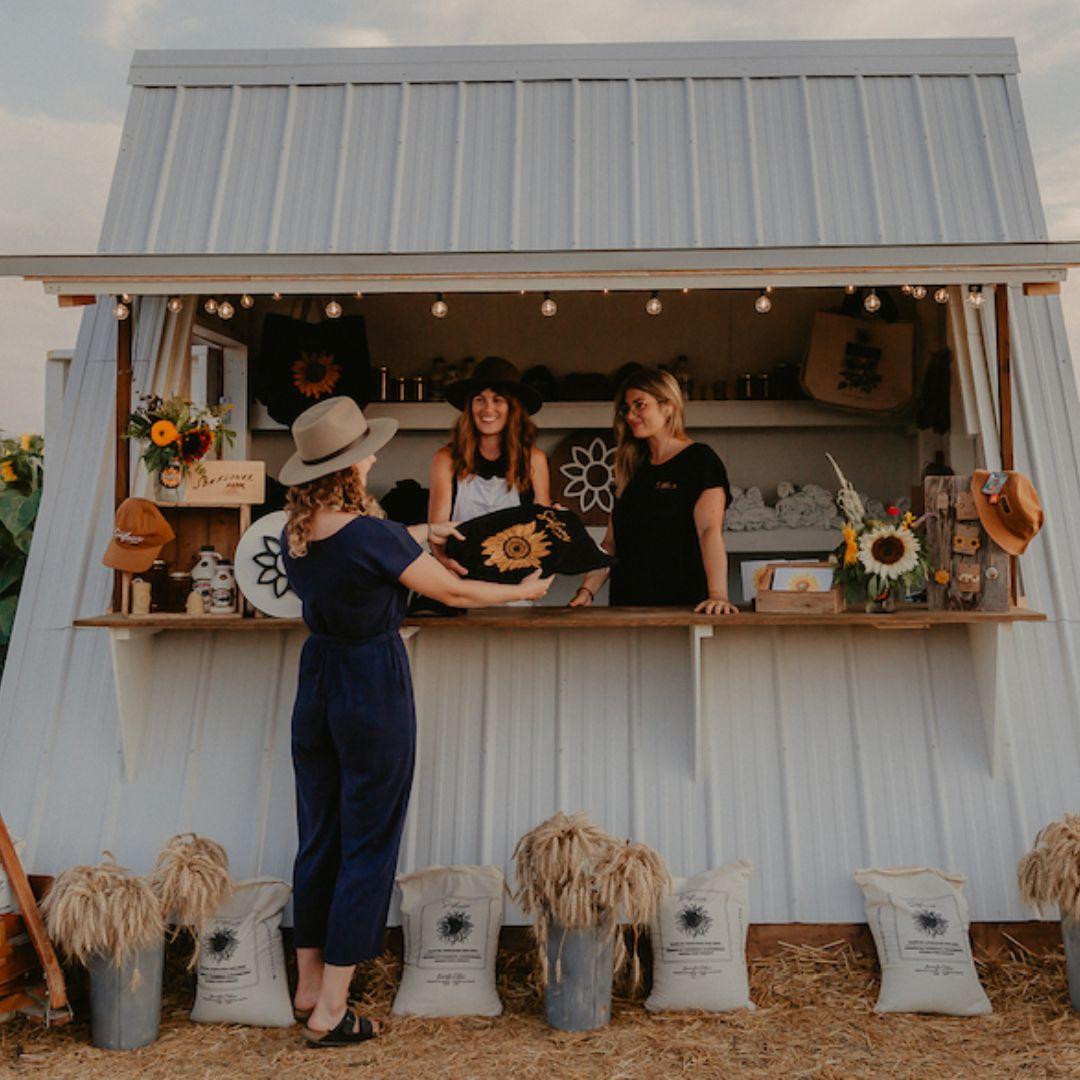 Vendor stand with sunflower displays and two women behind the counter and one woman in front