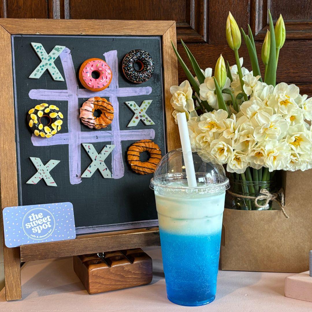 drink on a table with a tic tac toe board with donuts and a vase of flowers