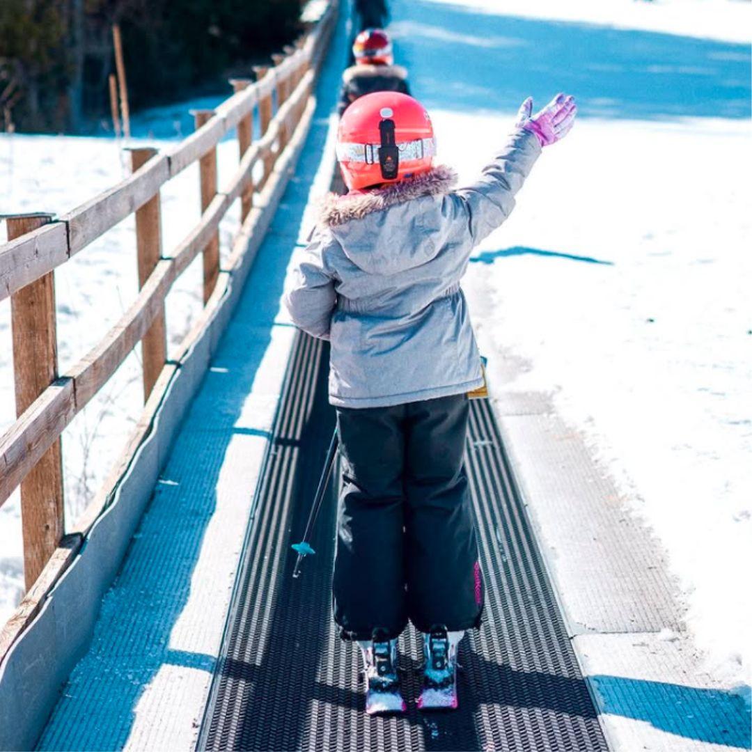 children going up ski hill on magic carpet lift
