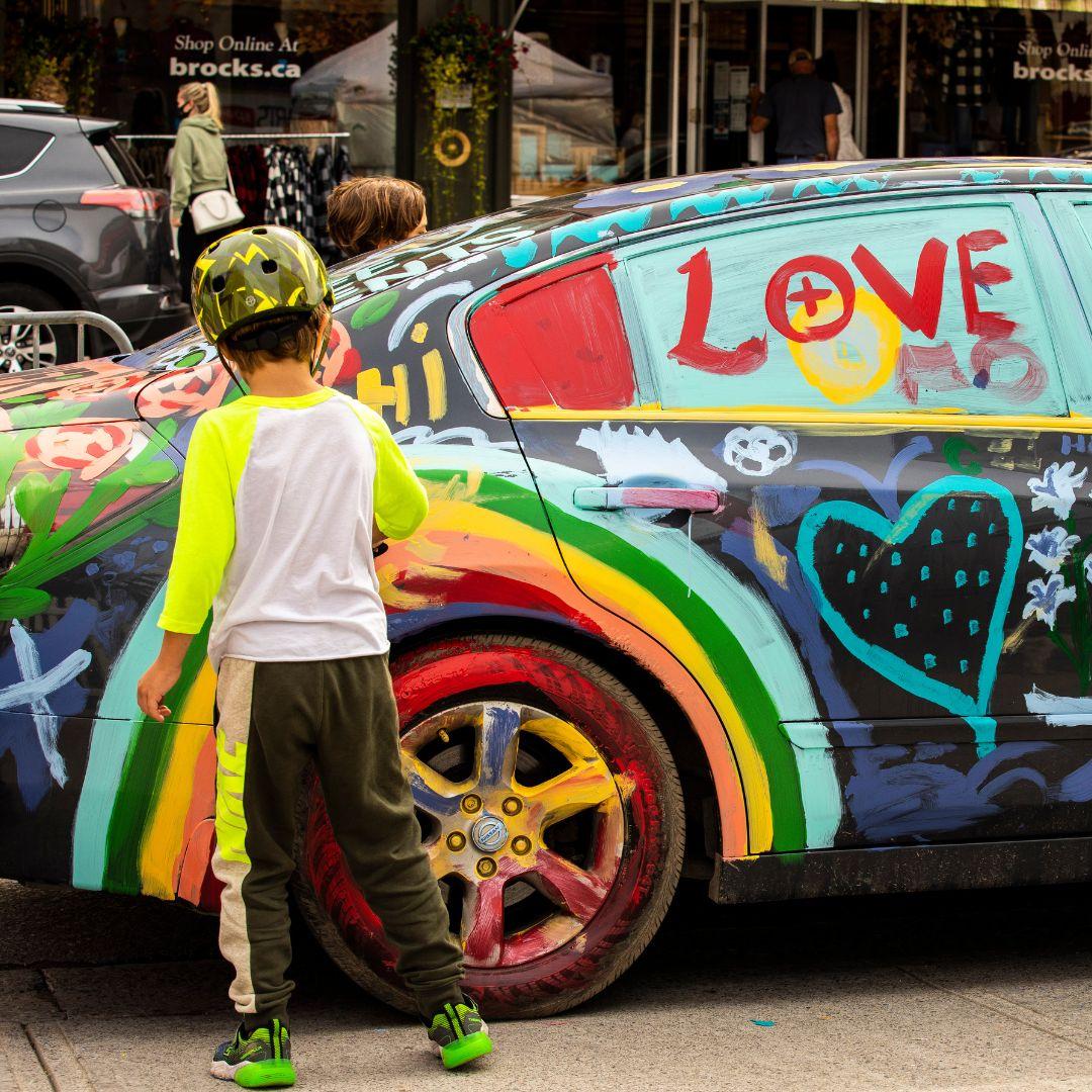 child stands in front of a colourfully painted car