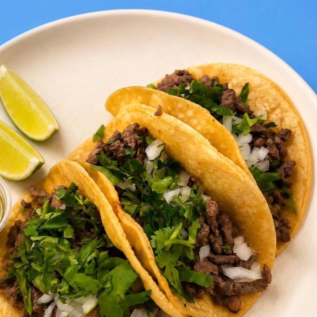Three tacos on a plate with two slices of lime on the side