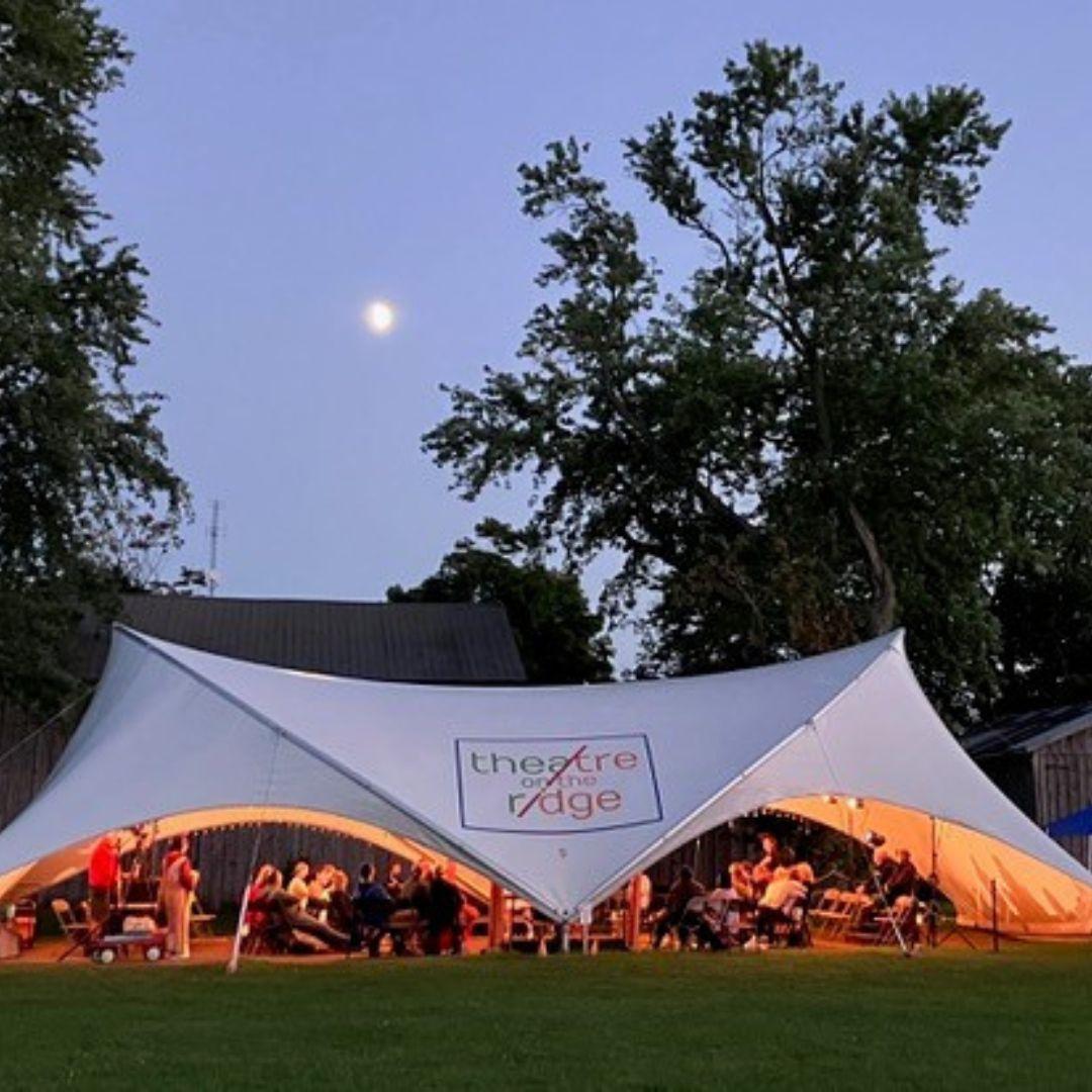 people seated under a tent at an outdoor theatre