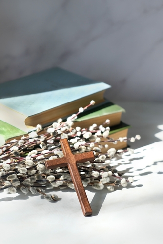 wooden cross_ old biblical books and willow twigs on table close up. Orthodox palm Sunday_ Easter holiday. Symbol of Christianity_ Lent_ Faith in God_ Church