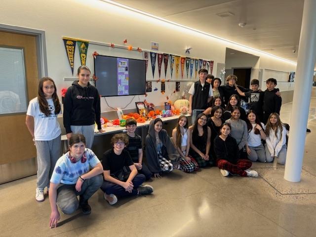 Multiple students pose in a hallway at Timnath Middle-High in front of and next to a table advertising Dia de los Muertos.